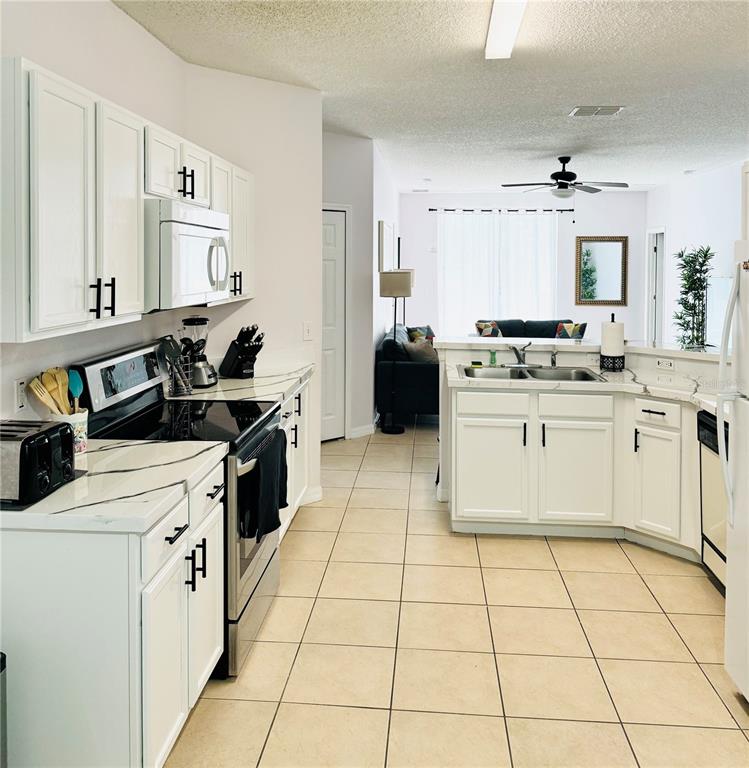A kitchen with white cabinets, black hardware, and marble-patterned countertops overlooks a living area — 1138 KNOLLWOOD DRIVE, DAVENPORT, FL