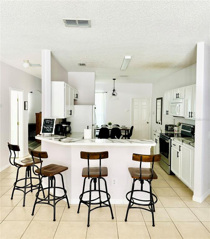 A kitchen features white cabinets, a breakfast bar with four stools, and tile flooring — 1138 KNOLLWOOD DRIVE, DAVENPORT, FL