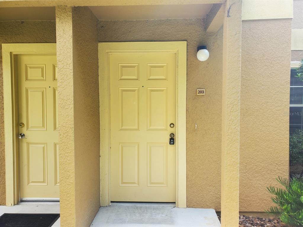 The exterior view shows a yellow front door labeled 203 with a lockbox attached — 5903 WILLOW RIDGE DRIVE UNIT 203, ZEPHYRHILLS, FL