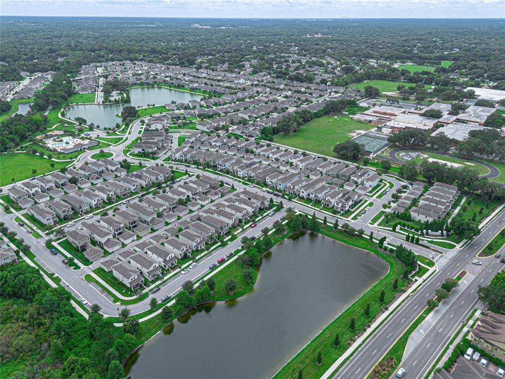 An aerial view shows a residential neighborhood with houses, ponds, and a nearby school complex — 225 GENTLE BREEZE LANE, WINTER SPRINGS, FL