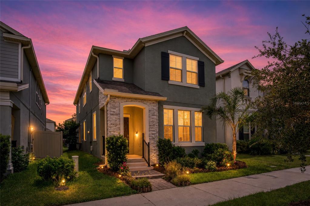 A two-story house with a stone-accented entryway and lit windows at sunset — 225 GENTLE BREEZE LANE, WINTER SPRINGS, FL