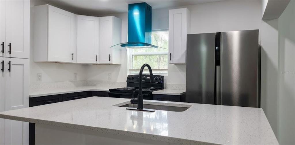 A modern kitchen features white cabinets, a quartz island, stainless steel appliances, and a blue hood — 210 S 15TH STREET, PALATKA, FL