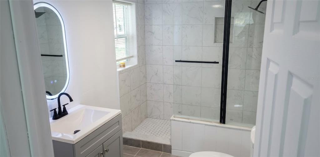 A bathroom features a gray vanity, an illuminated oval mirror, and a marble-tiled walk-in shower — 210 S 15TH STREET, PALATKA, FL