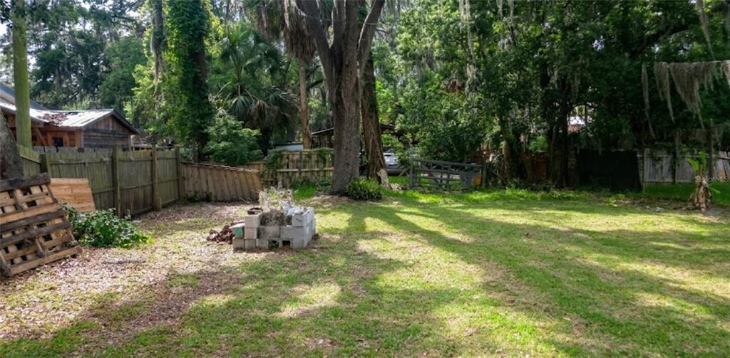 A grassy backyard features a wooden fence, a stack of concrete blocks, and large trees — 210 S 15TH STREET, PALATKA, FL