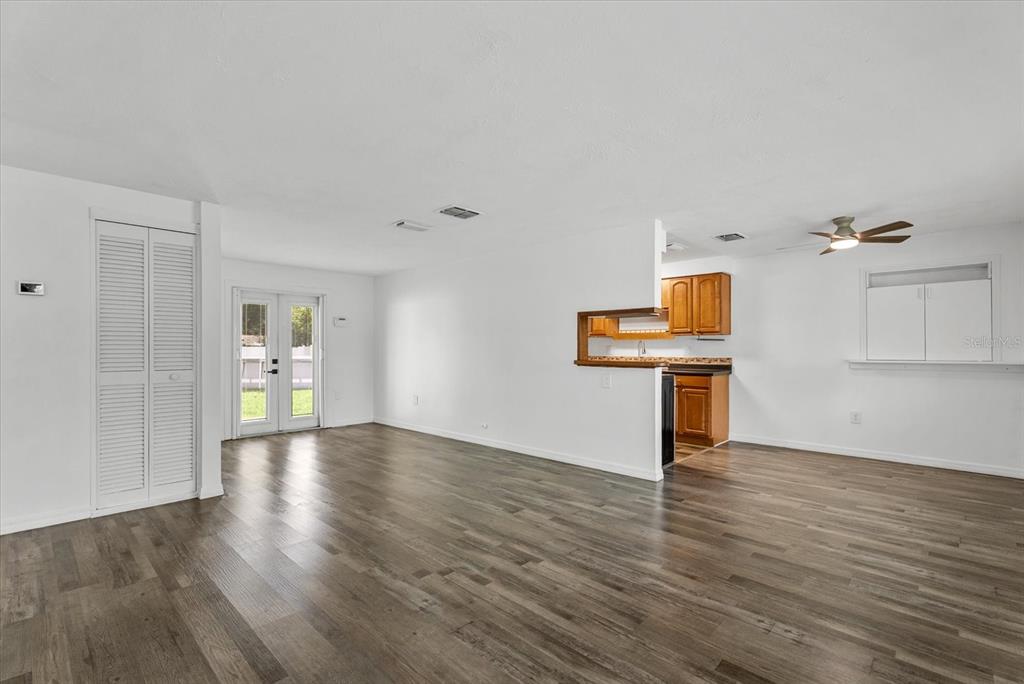 A bright living room features white walls, wood-look flooring, a ceiling fan, and a glass door — 4915 BELL MEADE DRIVE, SARASOTA, FL