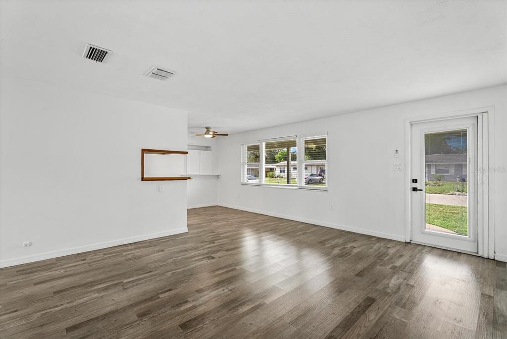 An open-concept living area features wood-look flooring, white walls, and a kitchen with wood cabinets — 4915 BELL MEADE DRIVE, SARASOTA, FL