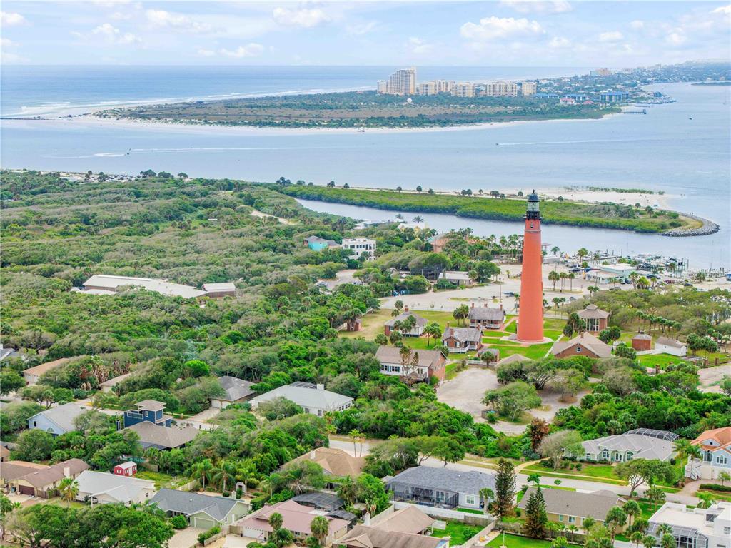An aerial view shows a tall red lighthouse surrounded by trees and residential homes — 70 OCEAN WAY DRIVE, PONCE INLET, FL