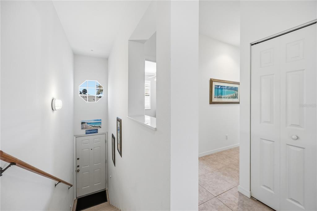 An entryway features a staircase, a white door, a pass-through window, and tiled flooring — 115 WOODBRIDGE DRIVE UNIT 201, VENICE, FL