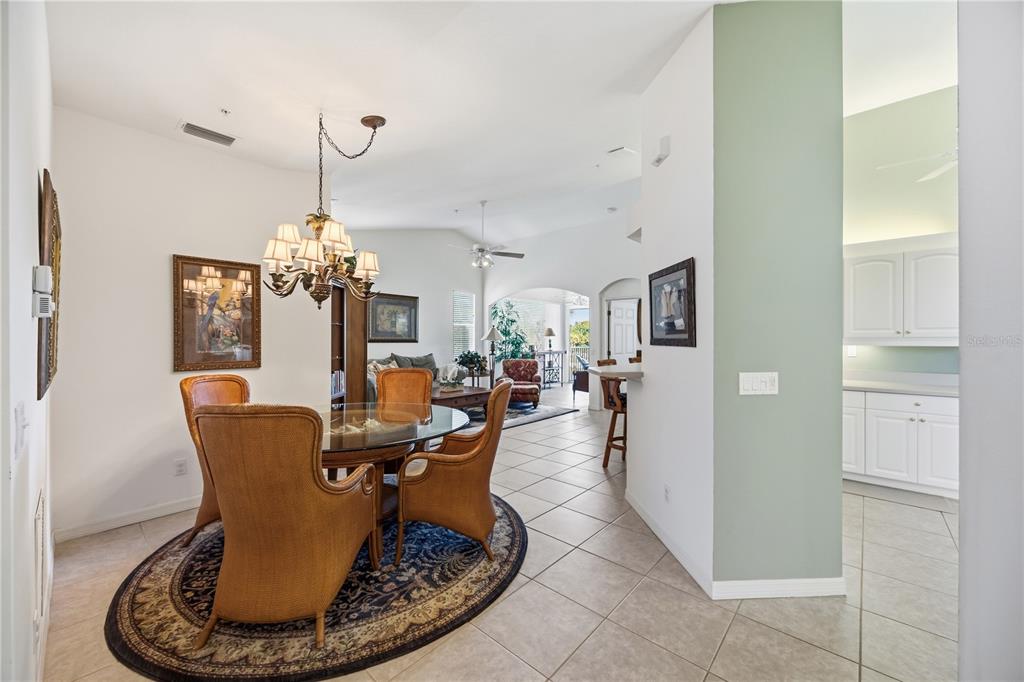 A dining area with a round glass table and wicker chairs opens into a living room — 115 WOODBRIDGE DRIVE UNIT 201, VENICE, FL
