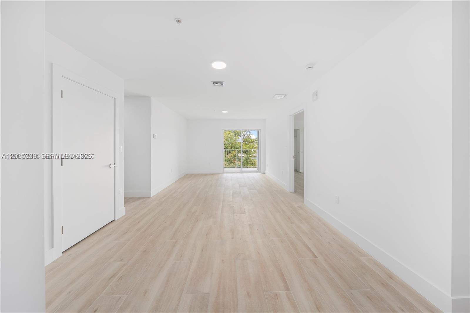 A bright, empty room features light wood-look flooring, white walls, and a sliding glass door — 32 NW 14th Ave # 4, Miami FL 33125, MIAMI, FL