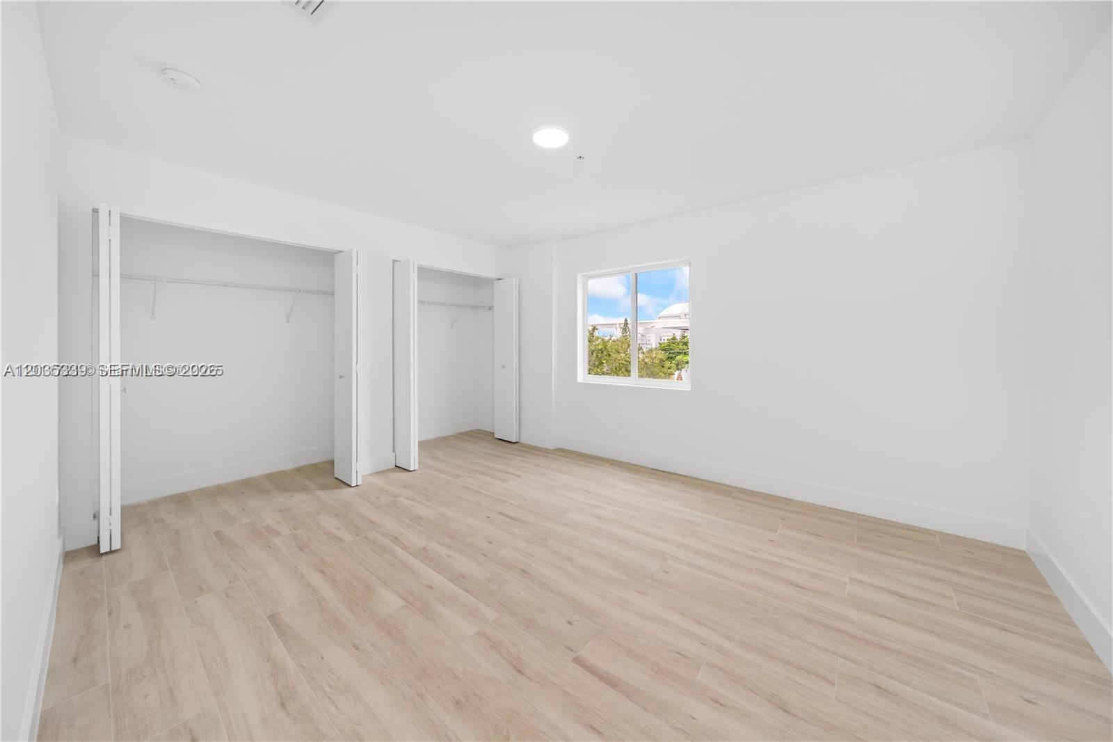An empty bedroom features white walls, light wood-look flooring, and two open closets — 32 NW 14th Ave # 4, Miami FL 33125, MIAMI, FL