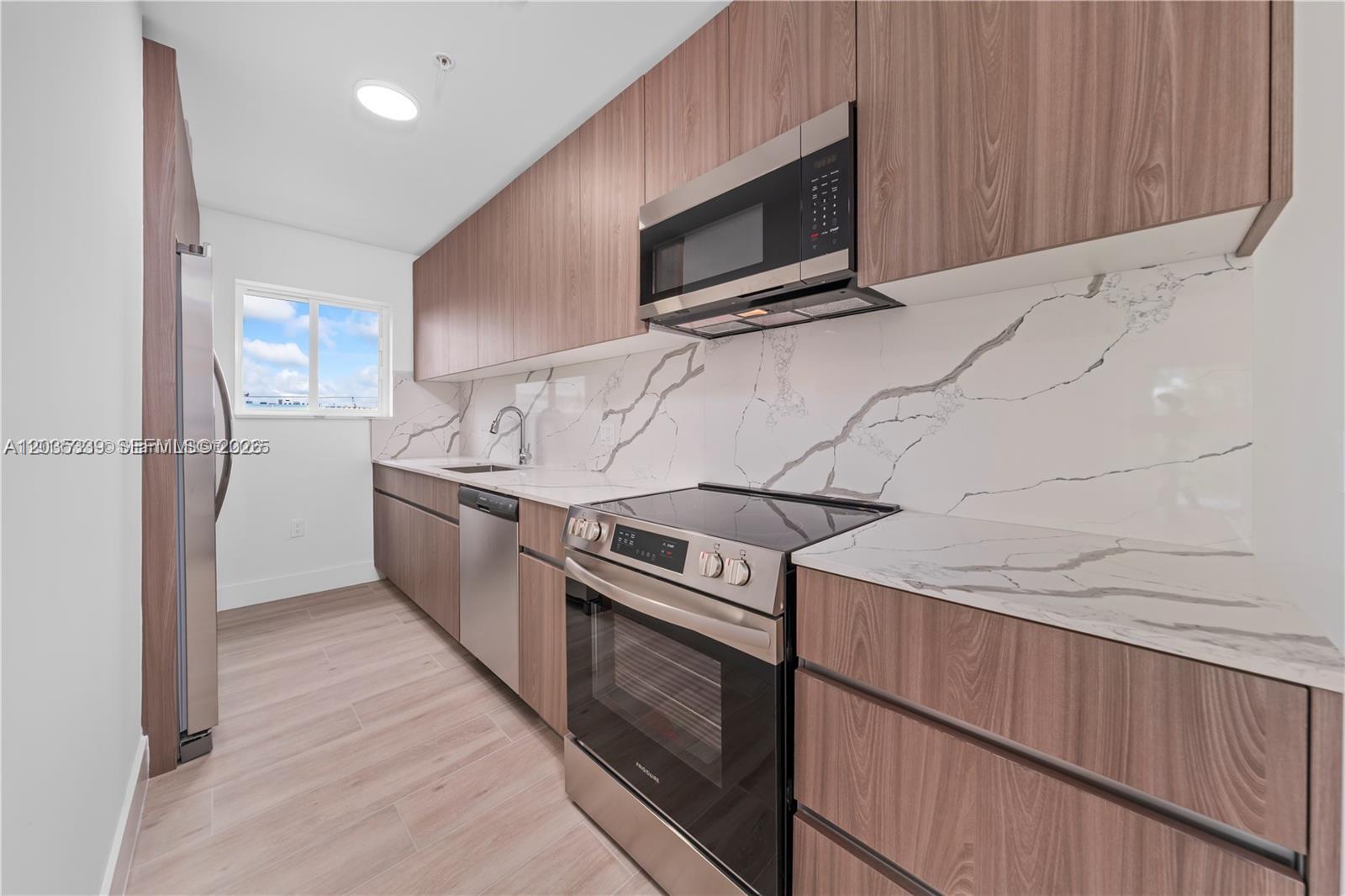 A modern kitchen features wood-grain cabinets, stainless steel appliances, and white marble-patterned countertops and backsplash — 32 NW 14th Ave # 4, Miami FL 33125, MIAMI, FL