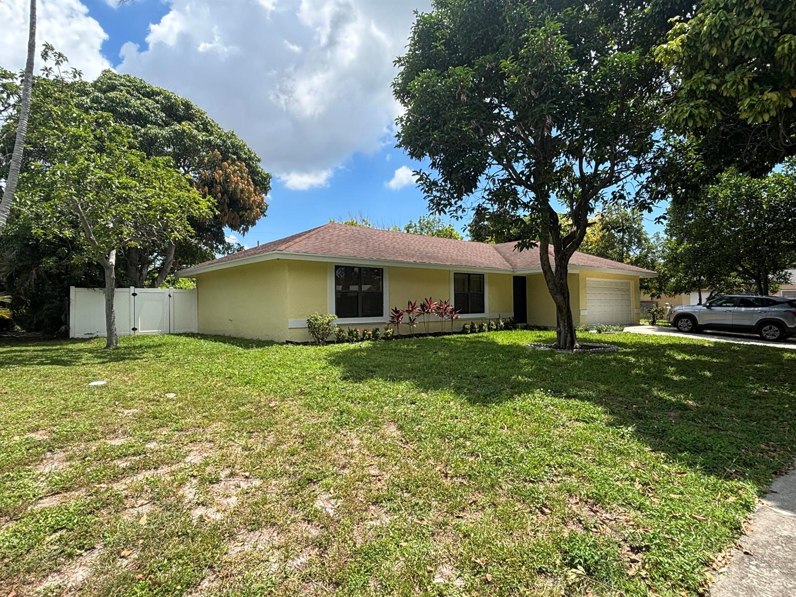 A yellow single-story house with a brown roof, a garage, and a large front yard — 1563 40th Street, West Palm Beach FL 33407, WEST PALM BEACH, FL