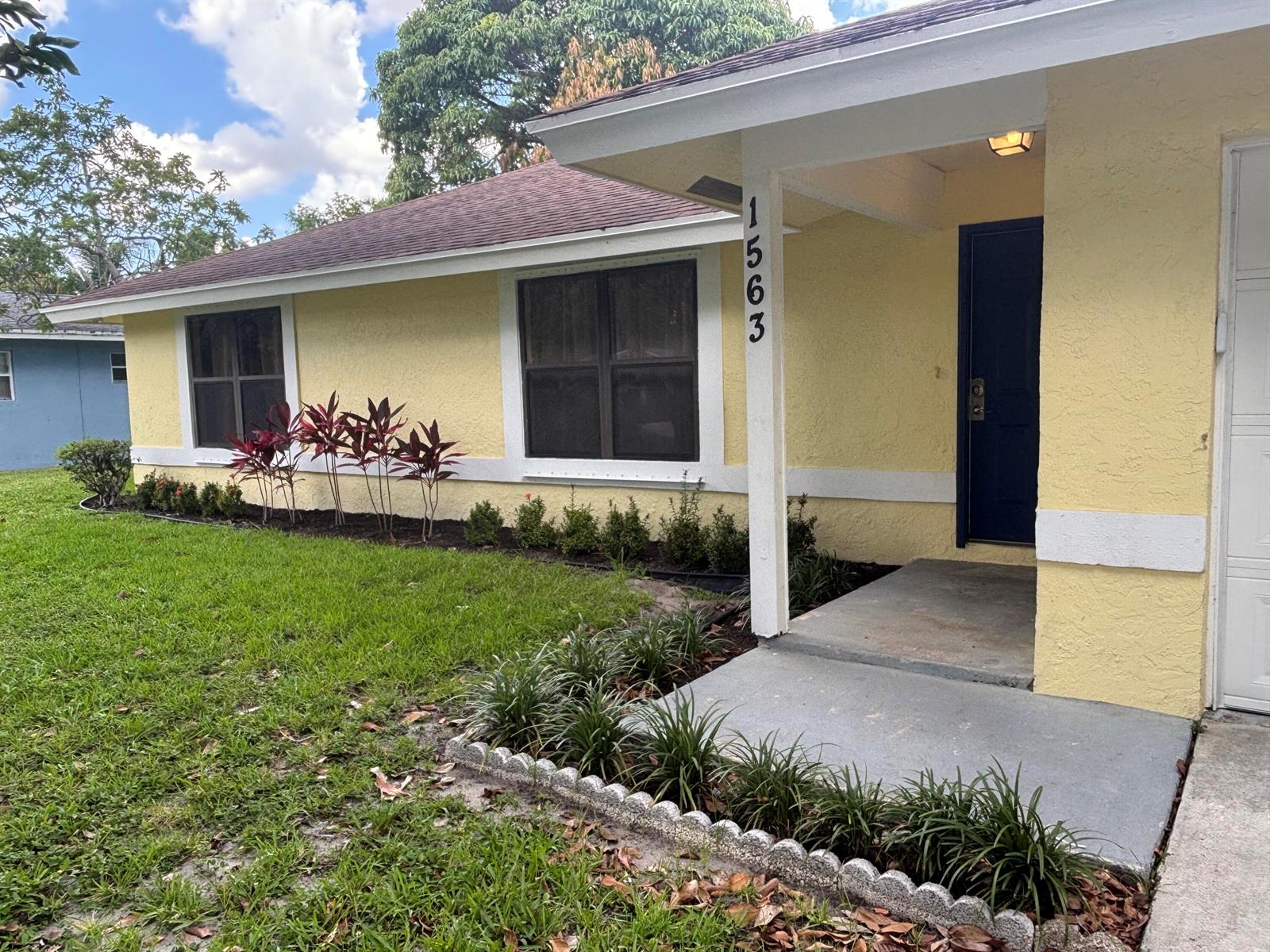 A yellow single-story house features a dark blue front door and a landscaped front yard — 1563 40th Street, West Palm Beach FL 33407, WEST PALM BEACH, FL