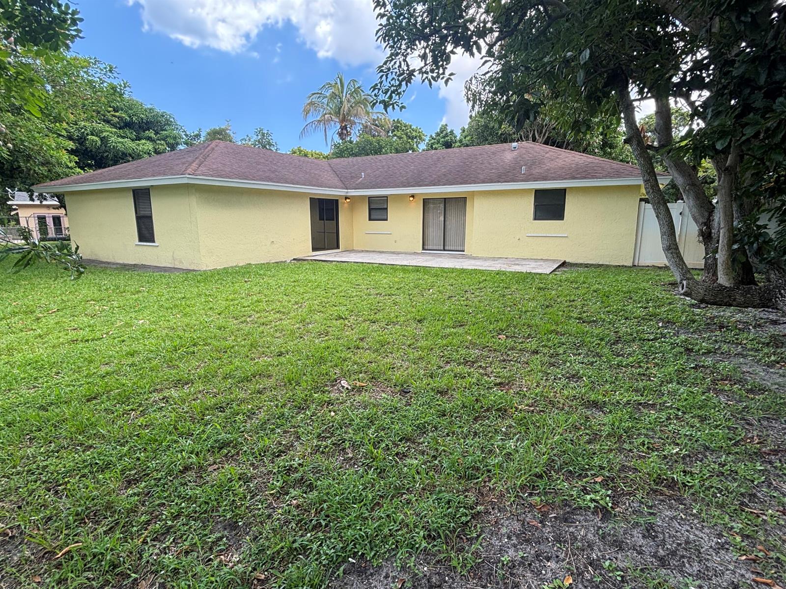 The backyard of a yellow house features a concrete patio and a grassy lawn — 1563 40th Street, West Palm Beach FL 33407, WEST PALM BEACH, FL