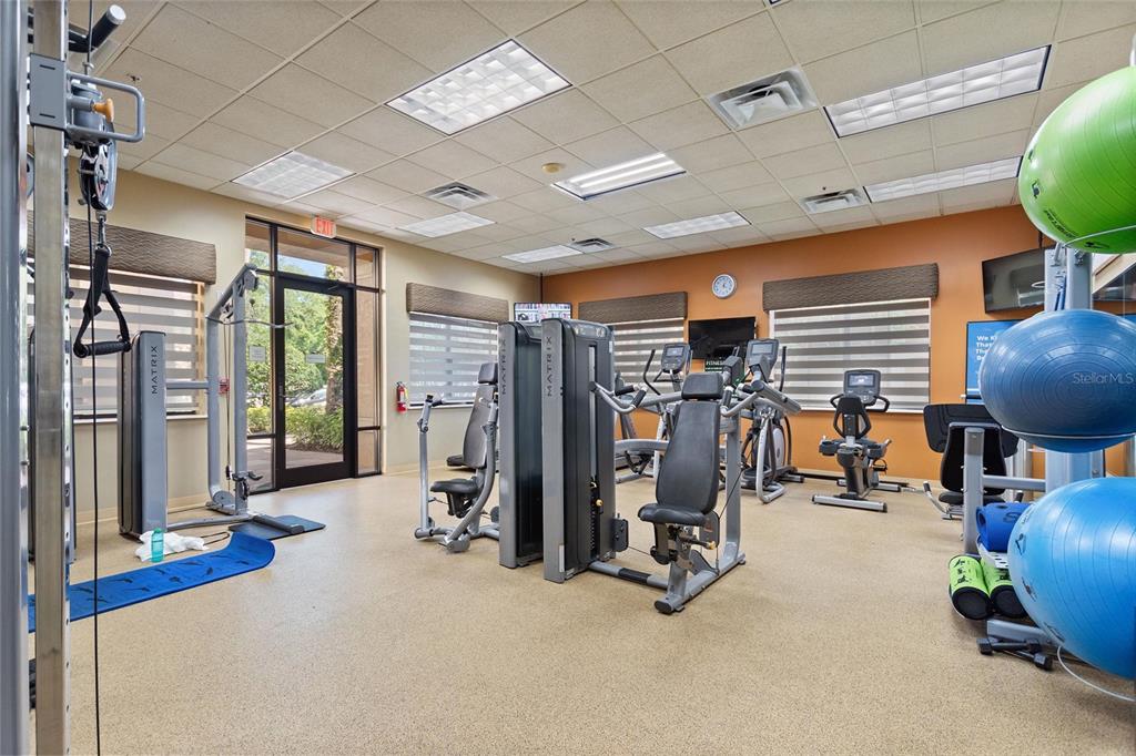 A gym room features multiple Matrix exercise machines, stability balls, and large windows with blinds — 12539 FLORIDAYS RESORT DRIVE UNIT 211D, ORLANDO, FL