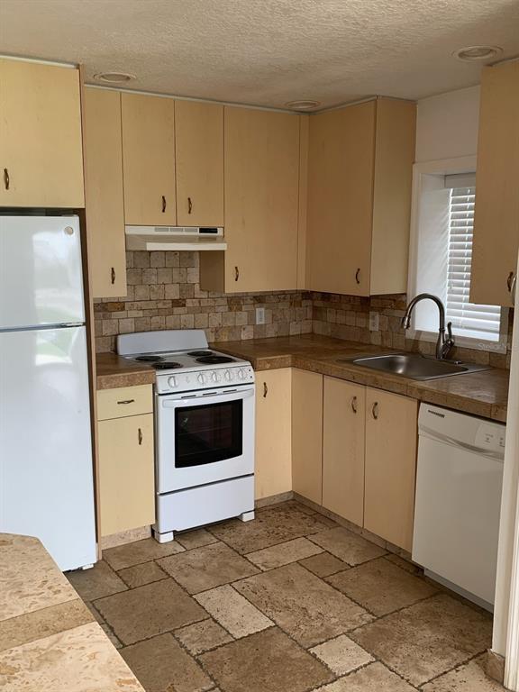 A kitchen features light wood cabinets, stone tile flooring, a stone backsplash, and white appliances — 1908 S OCEAN SHORE BOULEVARD UNIT B, FLAGLER BEACH, FL