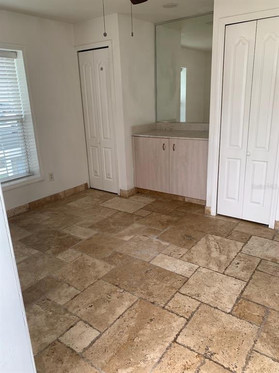 A room with travertine tile flooring, a built-in vanity with a mirror, and two closet doors — 1908 S OCEAN SHORE BOULEVARD UNIT B, FLAGLER BEACH, FL