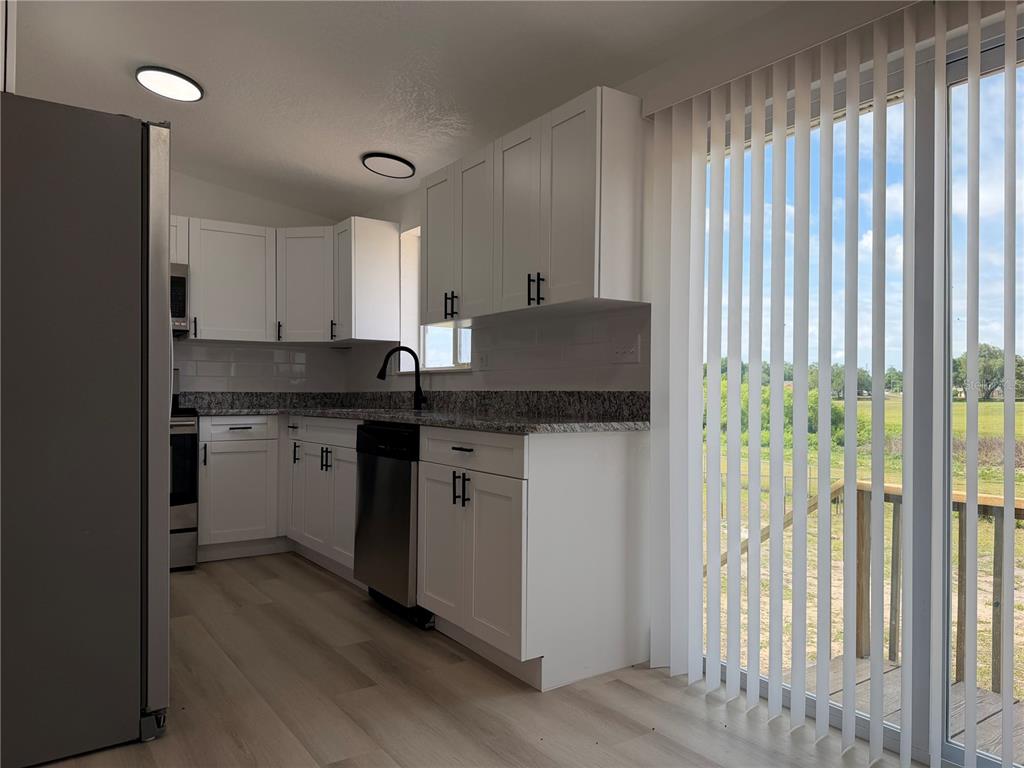 A kitchen features white cabinets, granite countertops, stainless steel appliances, and a sliding glass door — 514 GREENBROUGH DRIVE, LAKE WALES, FL