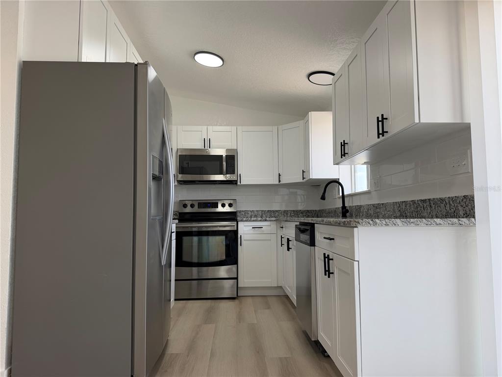 A kitchen features white cabinets, stainless steel appliances, granite countertops, and light wood-look flooring — 514 GREENBROUGH DRIVE, LAKE WALES, FL