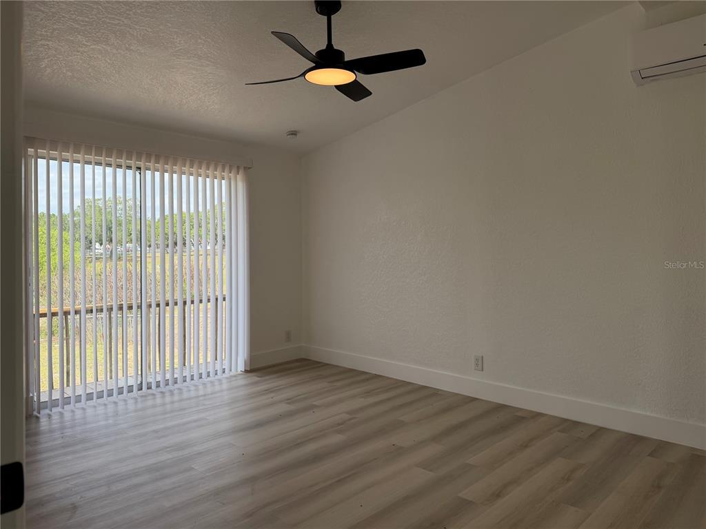 An empty room features light wood-look flooring, a ceiling fan, and vertical blinds on glass doors — 514 GREENBROUGH DRIVE, LAKE WALES, FL