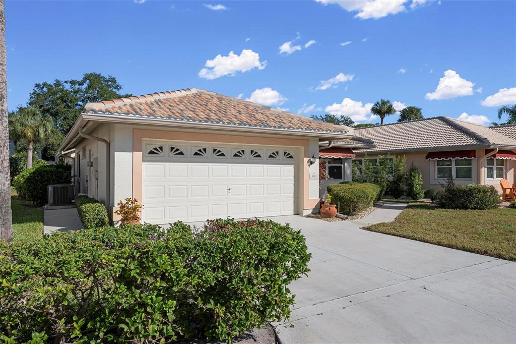 A single-story house with a white garage door, tan stucco walls, and a tiled roof — 4310 TURNBERRY COURT, BRADENTON, FL