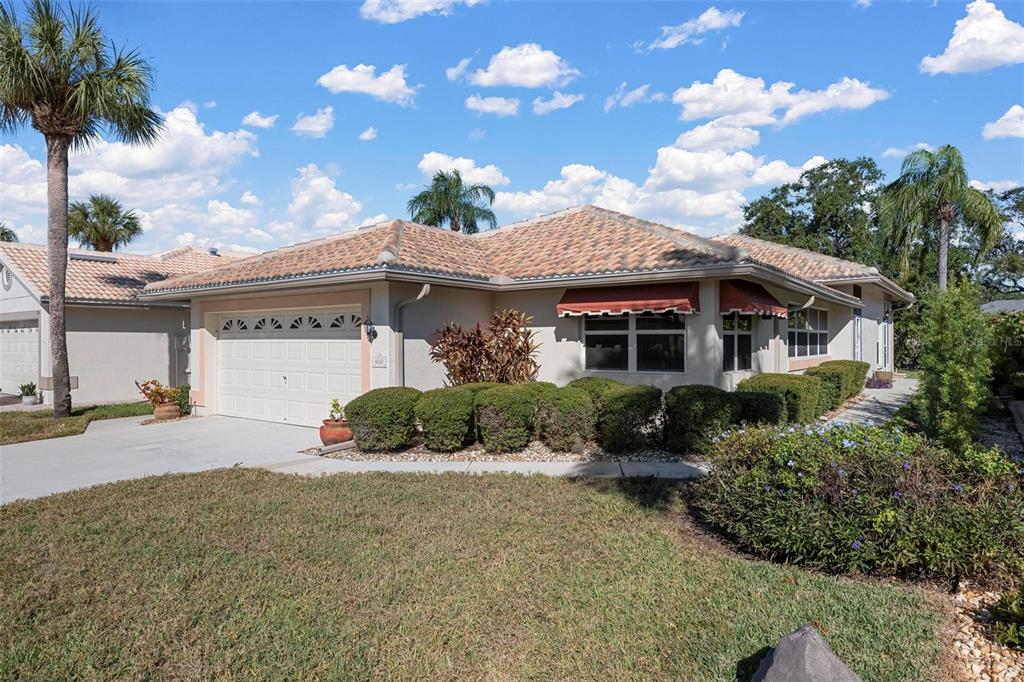 A single-story house with a tile roof, two-car garage, and manicured landscaping under a blue sky — 4310 TURNBERRY COURT, BRADENTON, FL
