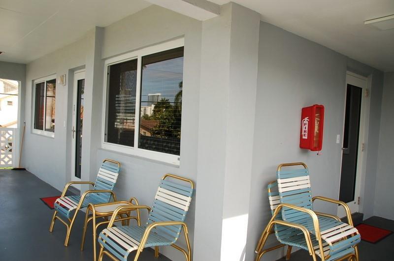 A covered outdoor walkway features light gray walls, blue and white lawn chairs, and a fire extinguisher — 600 Layne Boulevard # 201, Hallandale Beach FL 33009, HALLANDALE BEACH, FL