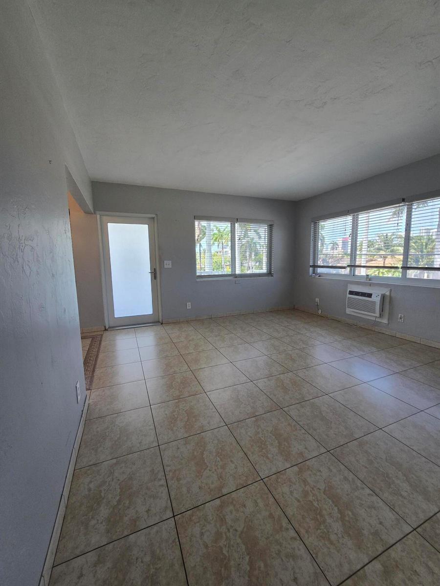 An empty room features light-colored tile flooring, gray walls, a glass door, and window blinds — 600 Layne Boulevard # 201, Hallandale Beach FL 33009, HALLANDALE BEACH, FL
