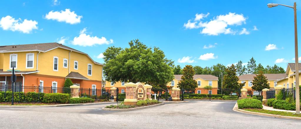 The exterior of a gated apartment complex features yellow buildings with orange accents and landscaping — 4086 WINDING VINE, LAKELAND, FL
