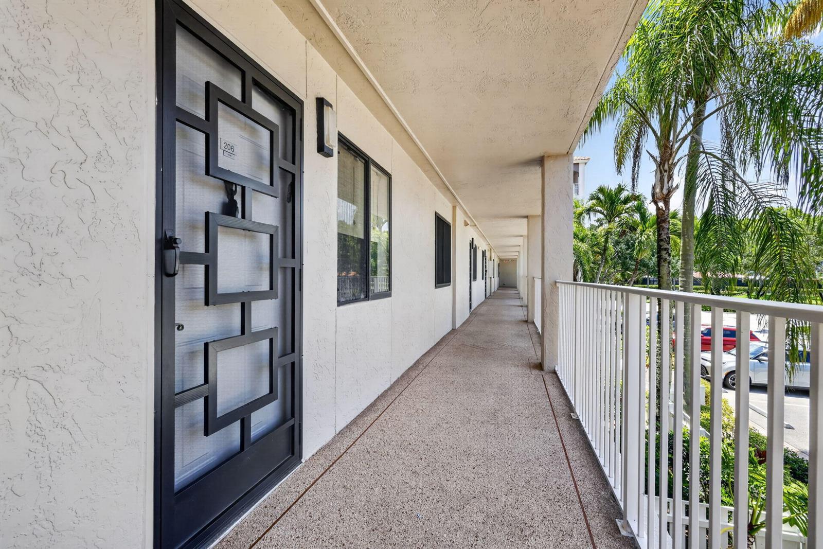 An exterior walkway with a patterned metal security door leads past apartment units — 6093 Pointe Regal Circle # 206, Delray Beach FL 33484, DELRAY BEACH, FL