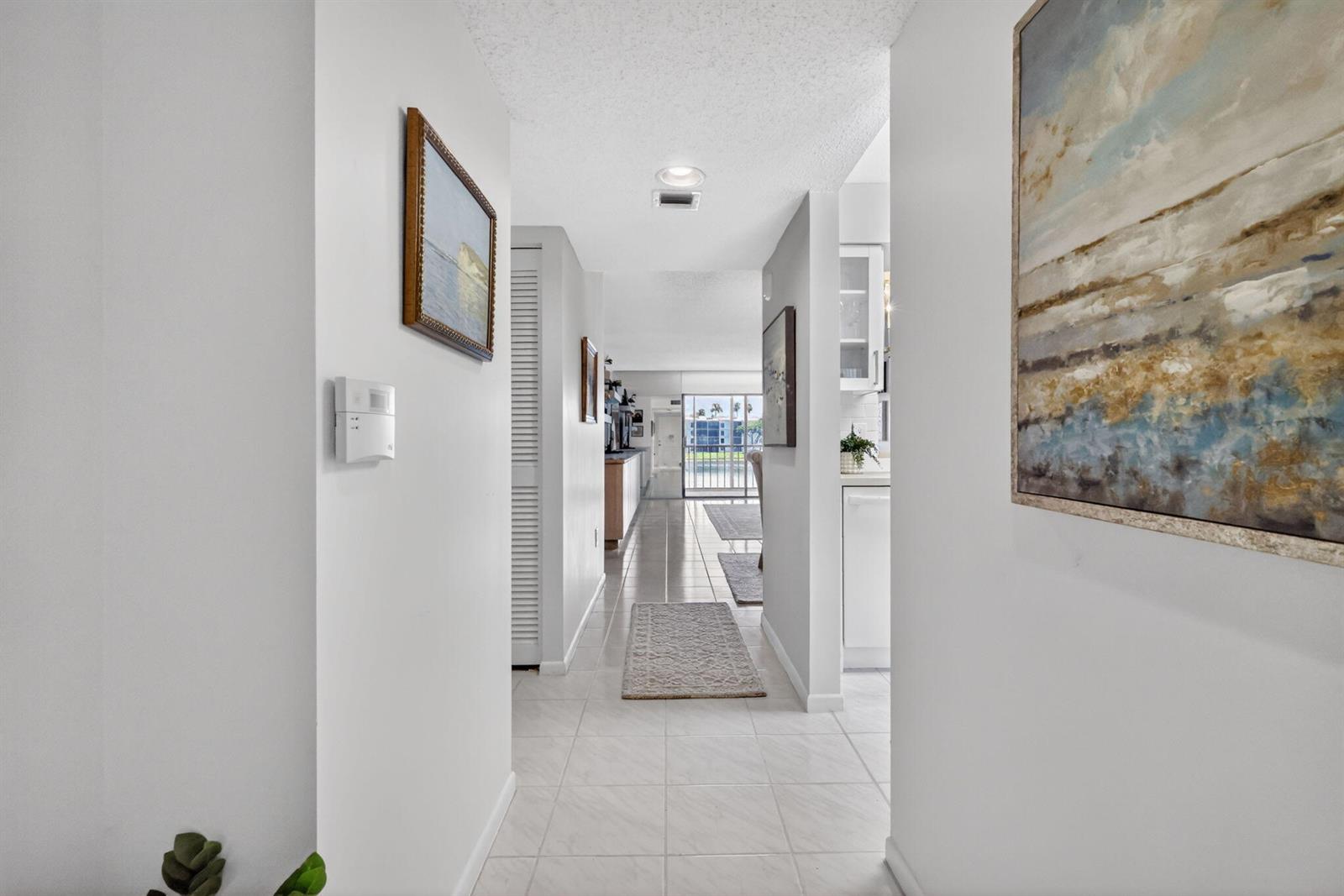 A bright hallway with white tile floors leads toward a living area with sliding doors — 6093 Pointe Regal Circle # 206, Delray Beach FL 33484, DELRAY BEACH, FL