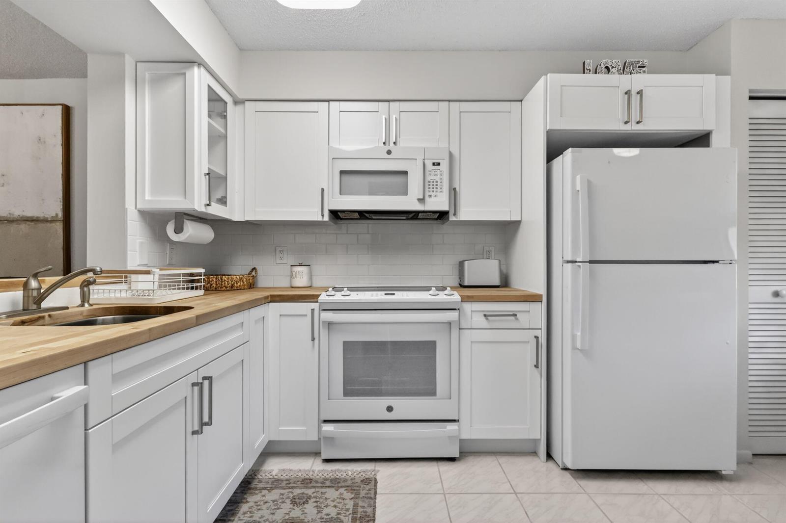 A kitchen features white cabinets, a wood countertop, and white appliances — 6093 Pointe Regal Circle # 206, Delray Beach FL 33484, DELRAY BEACH, FL