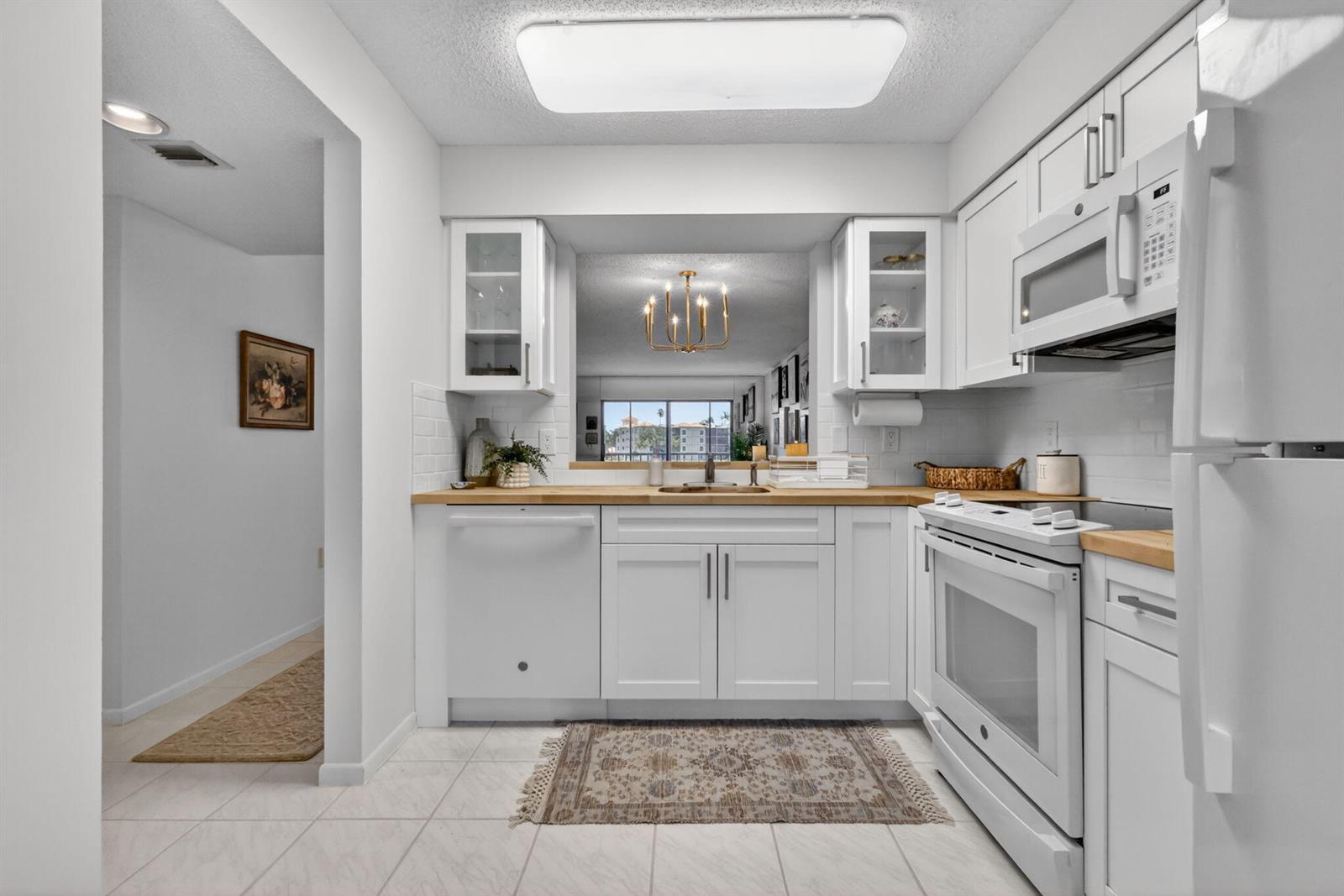A white kitchen features wood countertops, a pass-through window, and stainless steel appliances — 6093 Pointe Regal Circle # 206, Delray Beach FL 33484, DELRAY BEACH, FL