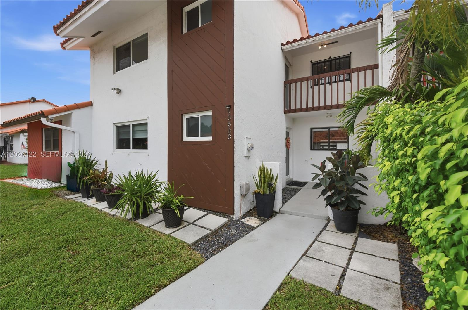 A two-story white stucco townhouse features a brown vertical accent wall and potted plants — 13523 SW 59th Ter, Miami FL 33183, MIAMI, FL