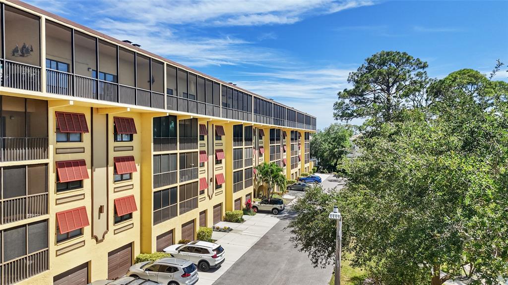 An exterior view of a multi-story yellow apartment building with screened balconies and parking — 5775 PARK STREET N UNIT 410, ST PETERSBURG, FL