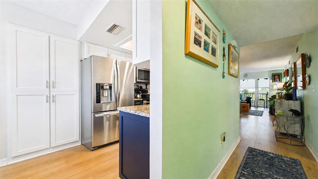 A kitchen with stainless steel appliances and white cabinets opens into a light green hallway — 5775 PARK STREET N UNIT 410, ST PETERSBURG, FL