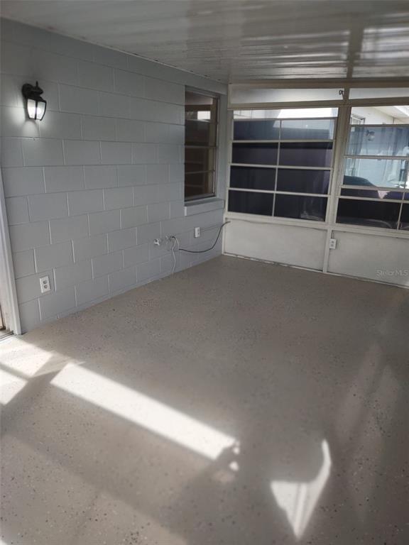 A covered patio with a light gray painted block wall, speckled flooring, and large windows — 13 LAKE VILLA WAY, KISSIMMEE, FL