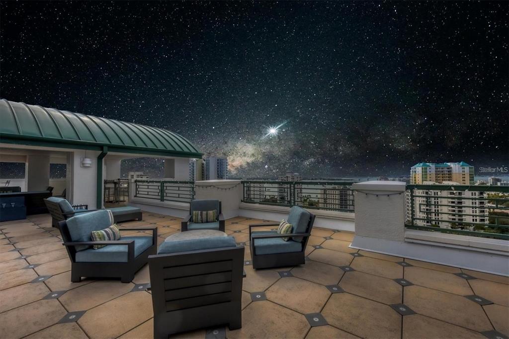 A rooftop terrace with outdoor seating overlooks a city skyline under a starry night sky — 505 S ORANGE AVENUE UNIT 301, SARASOTA, FL