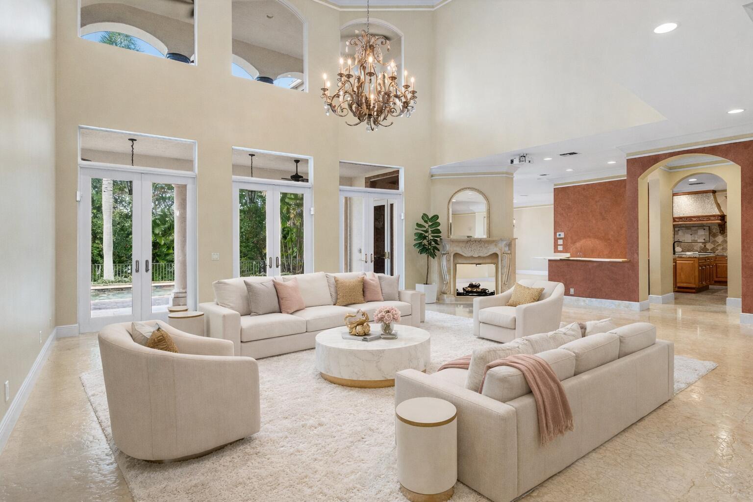 A spacious living room features high ceilings, a crystal chandelier, and neutral furniture on carpet — 4255 Gleneagles Drive, Boynton Beach FL 33436, BOYNTON BEACH, FL