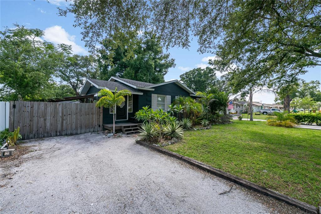 A dark green house with a gravel driveway and a wooden fence sits on a lawn — 1010 W BERRY AVENUE, TAMPA, FL