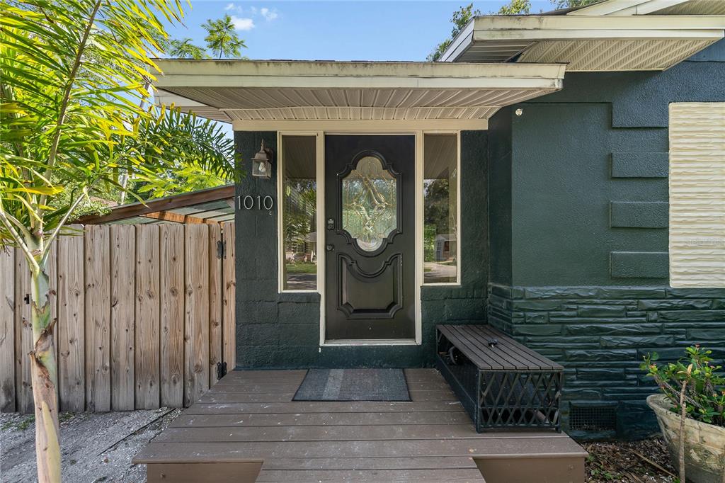 A dark-painted house entrance features a wooden porch, a glass-paneled door, and a side bench — 1010 W BERRY AVENUE, TAMPA, FL