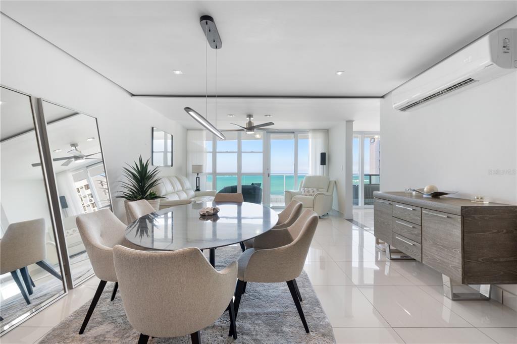 A dining area with a glass table and chairs overlooks the ocean through large windows — 5575 AVENIDA ISLA VERDE UNIT 904, CAROLINA, PR