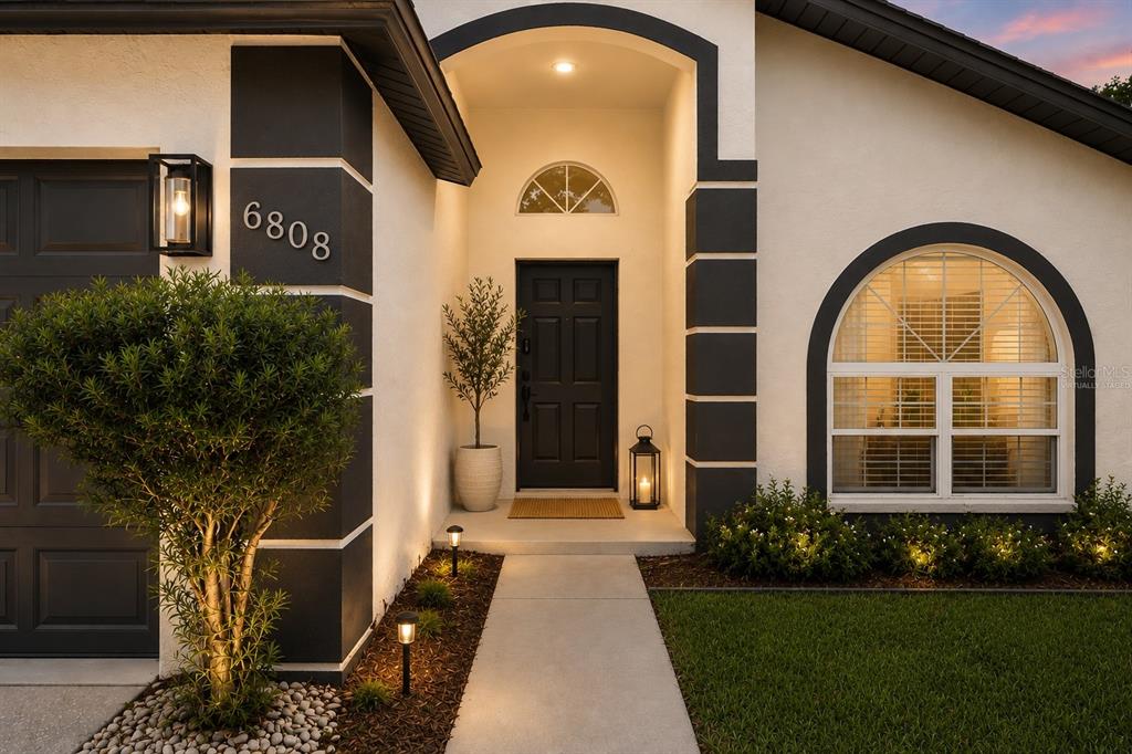 The exterior of a house features a dark front door, arched window, and landscaped walkway — 6808 YARDLEY OAKS COURT, TAMPA, FL