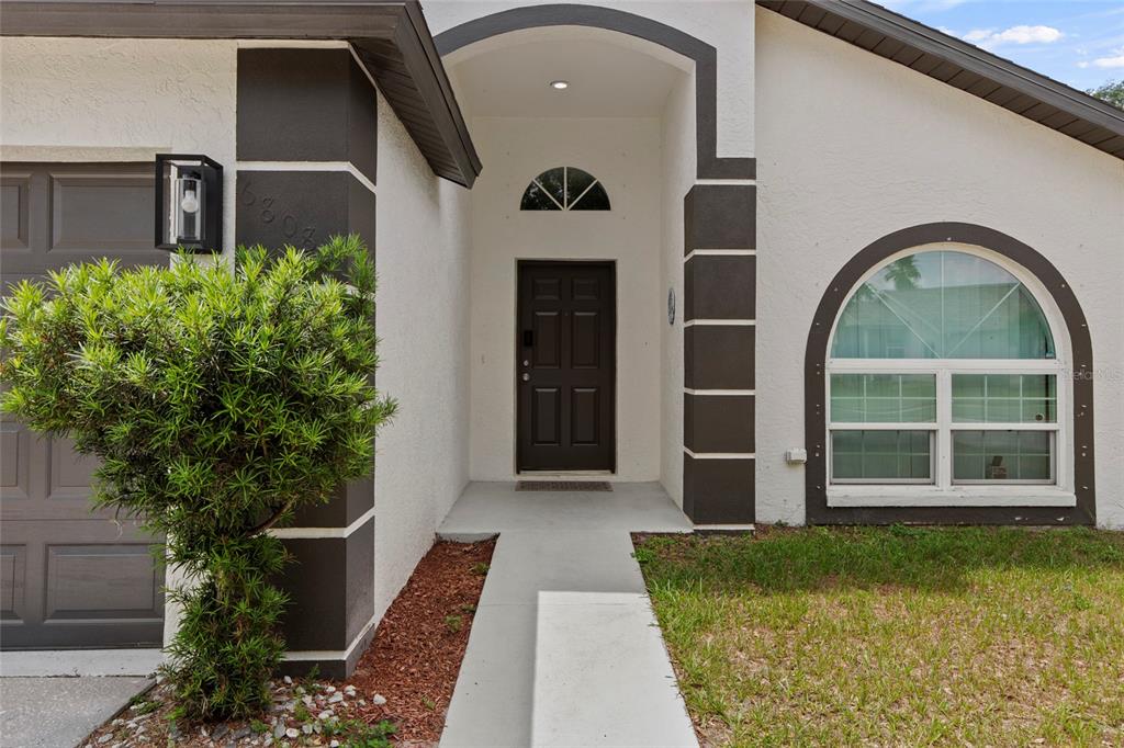 The exterior of a house features a dark front door, arched window, and stucco siding — 6808 YARDLEY OAKS COURT, TAMPA, FL