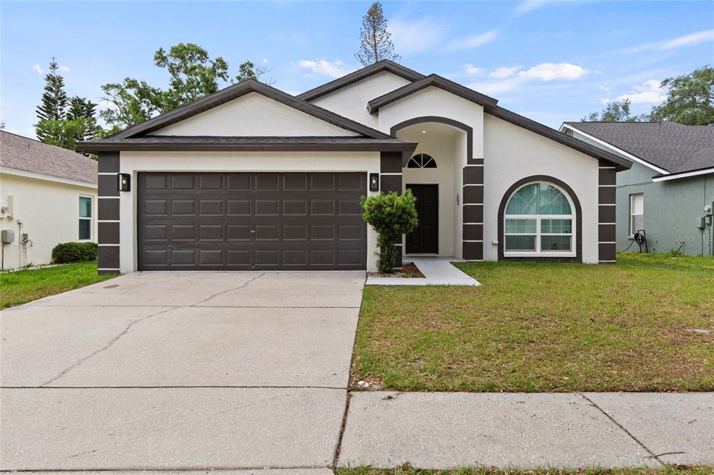 A single-story house with a dark brown garage door, arched window, and white stucco exterior — 6808 YARDLEY OAKS COURT, TAMPA, FL