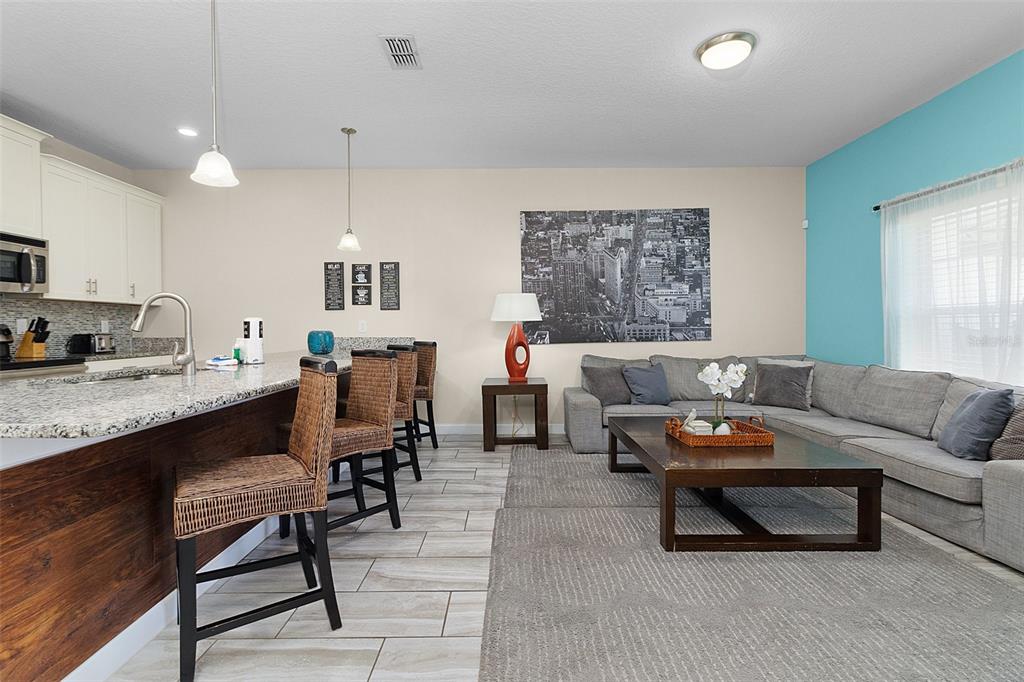 A kitchen with a granite island and bar stools opens into a living room area — 3148 PEQUOD PLACE, KISSIMMEE, FL
