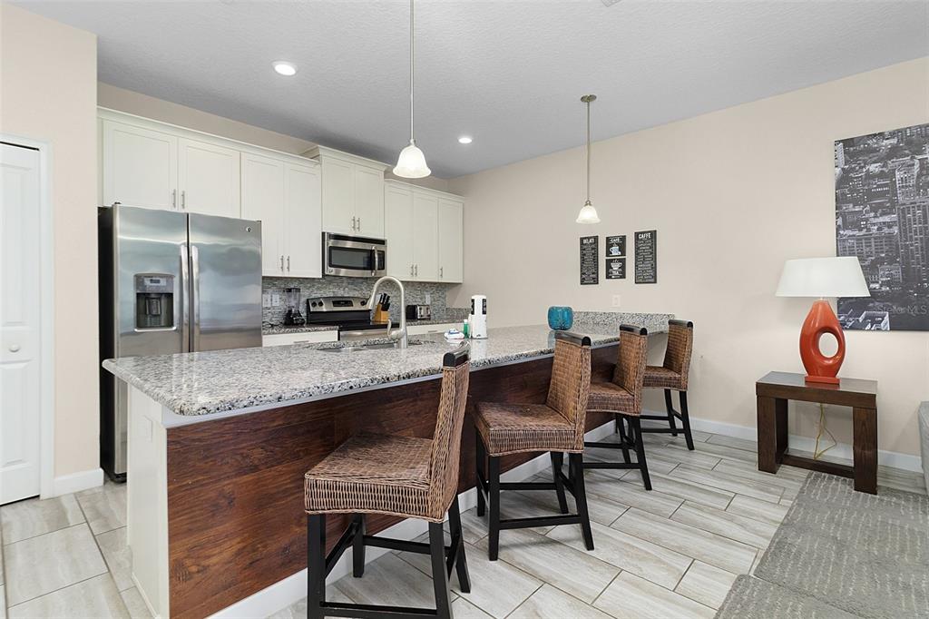 A kitchen features a granite-topped island with wicker bar stools and white cabinetry — 3148 PEQUOD PLACE, KISSIMMEE, FL