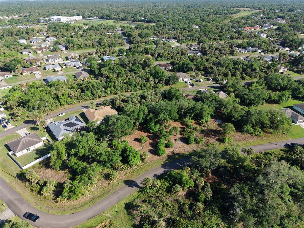An aerial view shows a vacant, wooded residential lot situated between suburban houses and streets — GOSHEN ROAD, NORTH PORT, FL