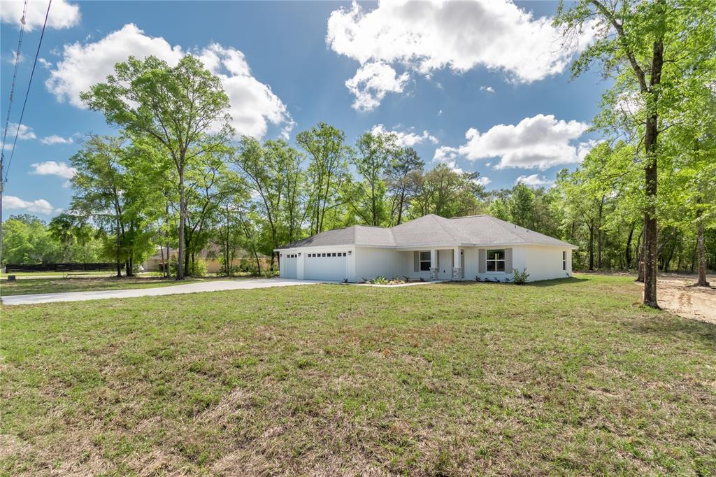 A white single-story house with a two-car garage sits on a large, grassy lot — 12440 SW 52ND LANE ROAD, OCALA, FL
